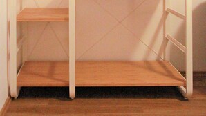 A white metal shelving unit with wooden shelves, a ladder, and a hanging cloth rack.