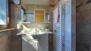 A bathroom with a marble sink, a mirror, a towel rack, and a clock on the wall.