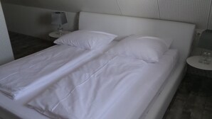 A neatly made bed with white linens and pillows, a bedside table with a lamp, and a wall with a perforated pattern.