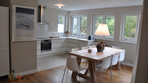 Une cuisine moderne avec des meubles blancs, une table à manger en bois et une grande fenêtre qui laisse entrer la lumière naturelle.