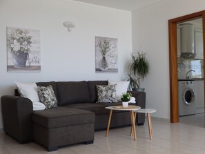 Uma sala de estar moderna com um sofá seccional, uma mesinha redonda e duas luminárias fixadas na parede.