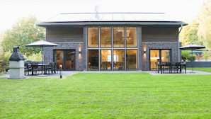 A modern building with large windows and a patio area with outdoor seating. - Villa Thormarcon, Plauer See, 20 Gäste, Sauna+Pool (Malchow)