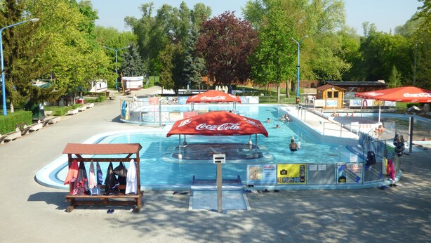 A swimming pool area with Coca-Cola branded umbrellas, a small wooden structure, and a paved walkway.