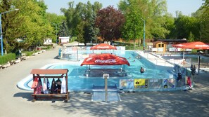 A swimming pool area with Coca-Cola branded umbrellas, a small wooden structure, and a paved walkway.