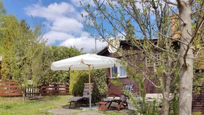 A wooden cabin with a patio area featuring two lounge chairs and a table, surrounded by a wooden fence and a garden.