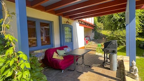 A covered patio area with a red sofa, a table, and a barbecue grill.