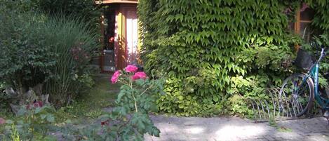 A garden with a brick pathway, pink flowers, and a bicycle leaning against a wall.