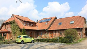 Uma casa de dois andares com telhado inclinado, painéis solares e um carro estacionado na entrada.