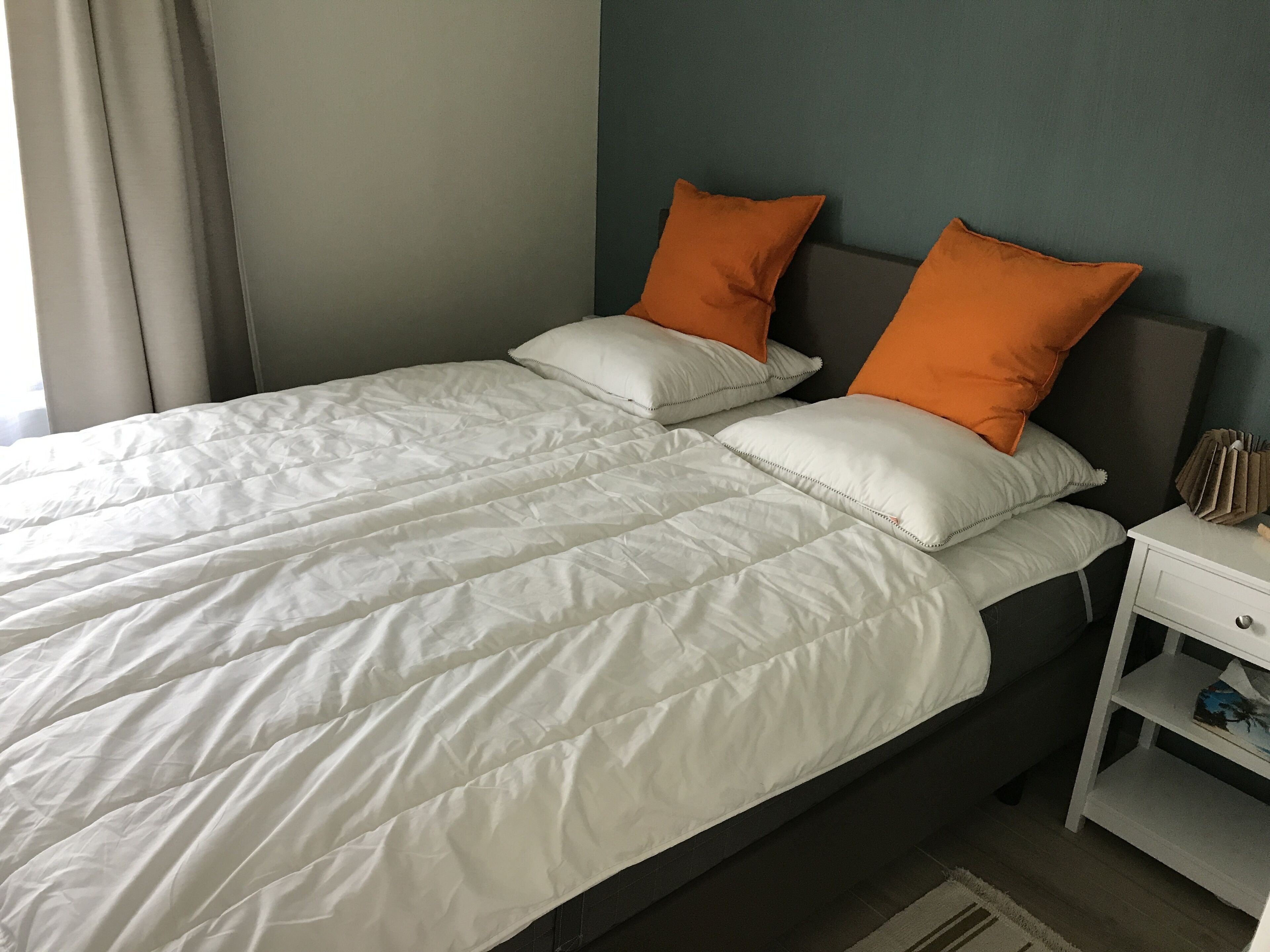 Ein Doppelbett mit weißen und orangefarbenen Kissen, einem weißen Nachttisch und einem dunklen Kopfteil.
