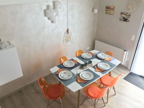 A dining area with a table set for four, orange chairs, and a hanging light fixture.