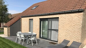 A brick house with a tiled roof, a patio with a table and chairs, and two lounge chairs. - Lovely vacation home, De Haan, 6 pers., completely renovated, child-friendly (De Haan)