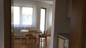 A narrow hallway with a wooden floor leading to a dining area with a table and chairs.