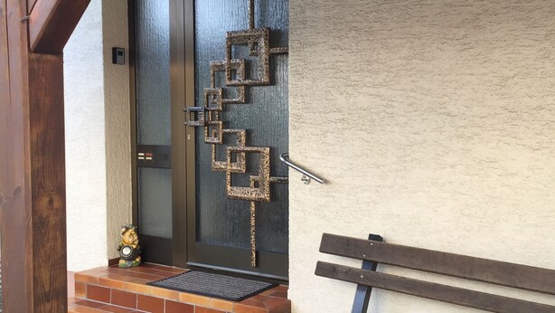 A wooden bench, a metal sculpture, and a door with a textured wall.