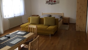 A cozy room with a yellow sofa, a wooden table with a keyboard, and a bed with a wooden headboard.