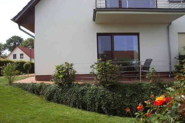 Una casa moderna de dos pisos con balcón, un área de comedor con mobiliario exterior y jardines bien cuidados.