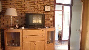 Ein Holzschrank mit einem Fernseher darauf, eine Uhr an der Wand und eine Tür zu einem anderen Raum.