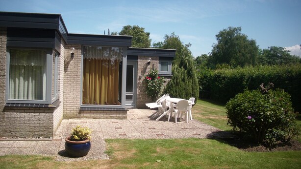Ein modernes Haus mit Ziegelaußenwand, einer Haustür und einer kleinen Terrasse mit weißen Stühlen und einem Tisch.