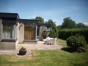 A modern house with a brick exterior, a front door, and a small patio with white chairs and a table. - Holiday house in a quiet location (Oosterend)