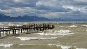 A wooden pier extending into turbulent waters with mountains in the background.