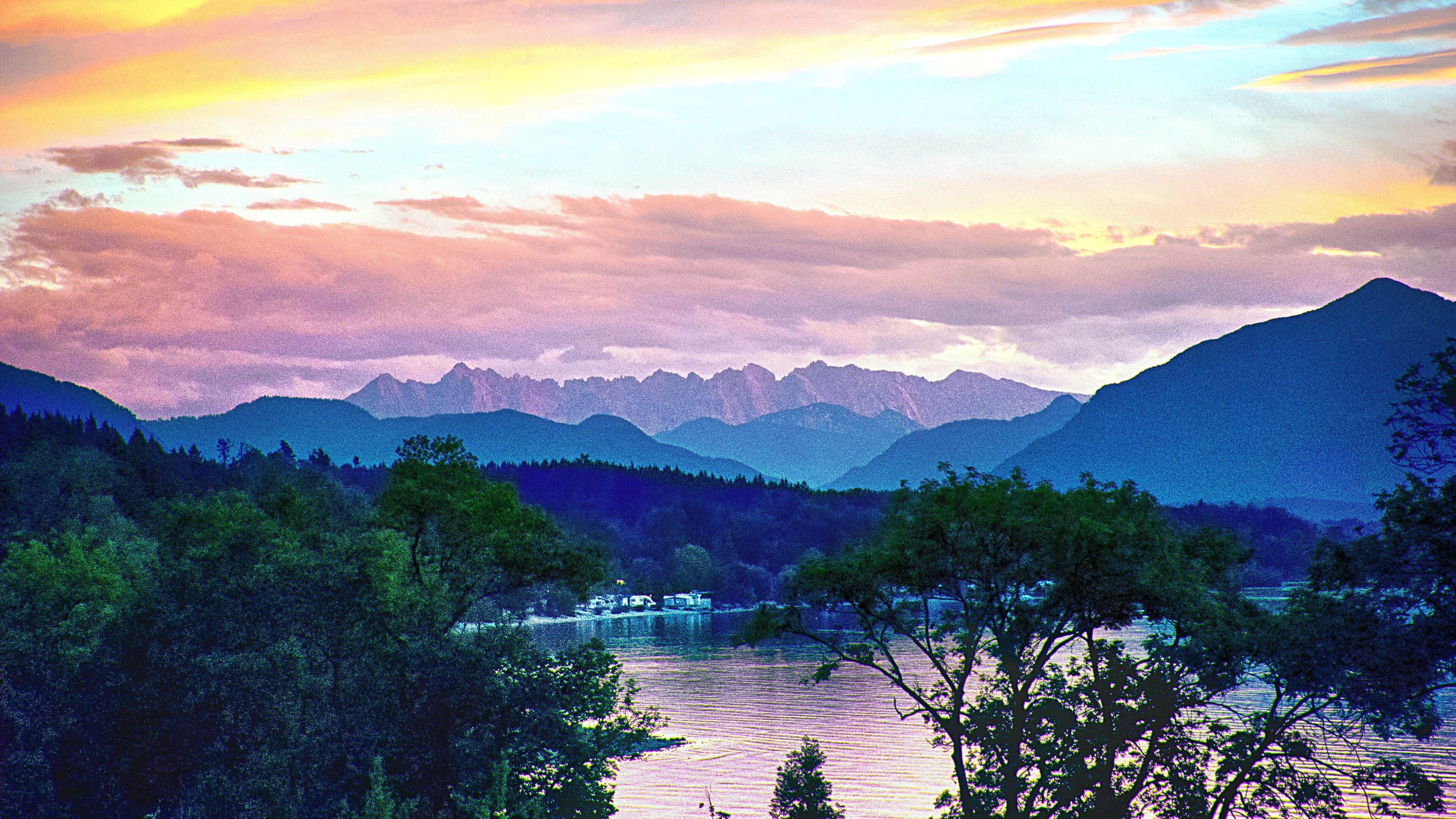 A mountainous landscape with a river and trees in the foreground.