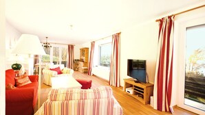A spacious living room with a large window, a television, and a dining area with wooden furniture.