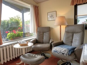 A room with two leather armchairs, a small table with a basket, a radiator, and a window with curtains.