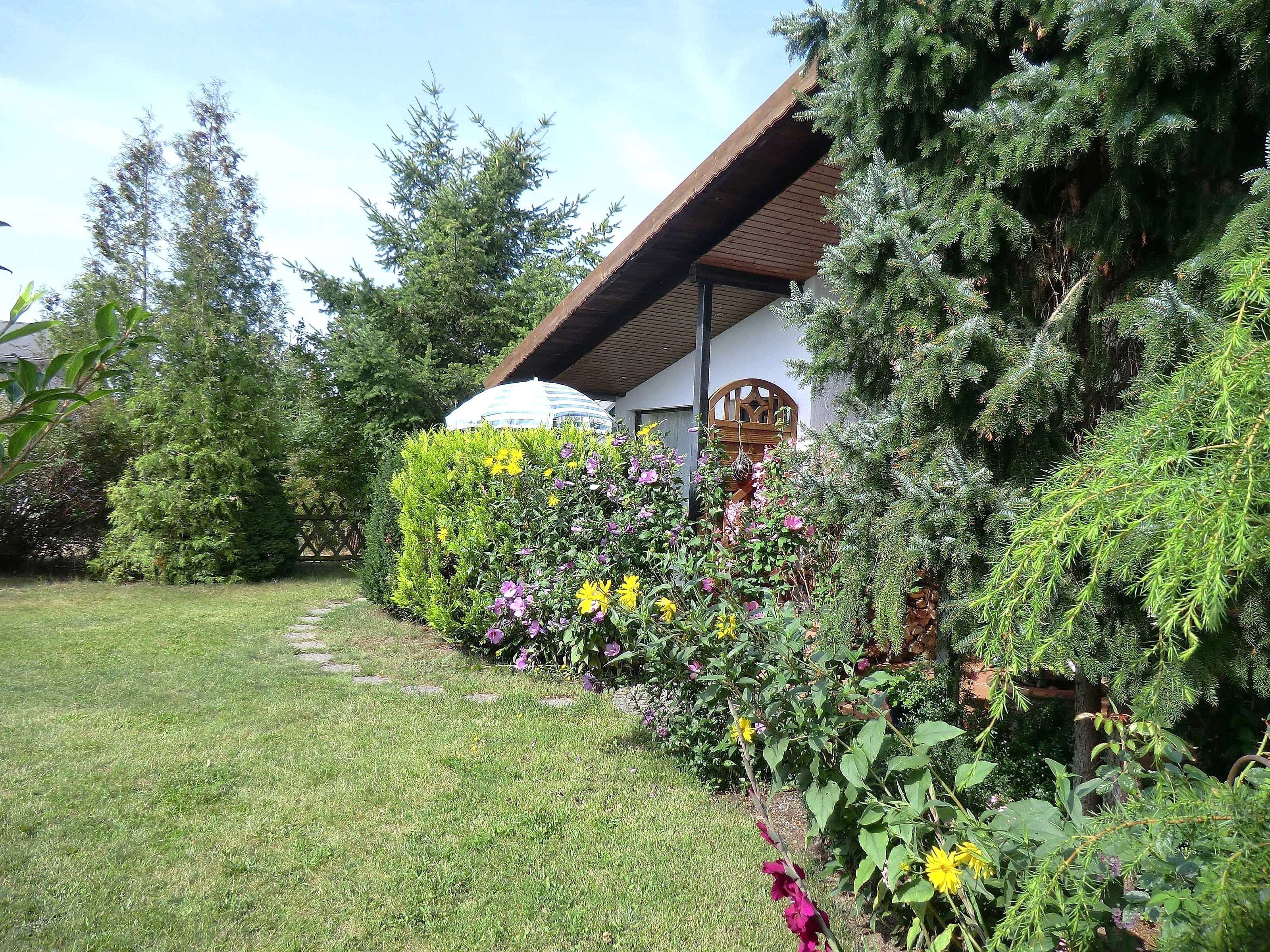 A well-maintained garden with a variety of plants and flowers, a wooden structure with a sloped roof, and a clear pathway.