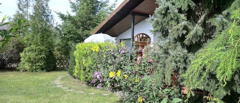 Un jardin bien entretenu, agrémenté de diverses plantes et fleurs, une structure en bois dotée d’un toit incliné et un chemin bien dégagé.