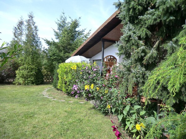 A well-maintained garden with a variety of plants and flowers, a wooden structure with a sloped roof, and a clear pathway.
