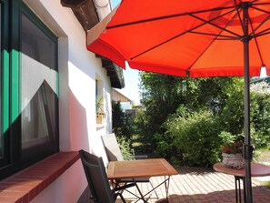 A patio area with a table and chairs, a red umbrella, and a potted plant.