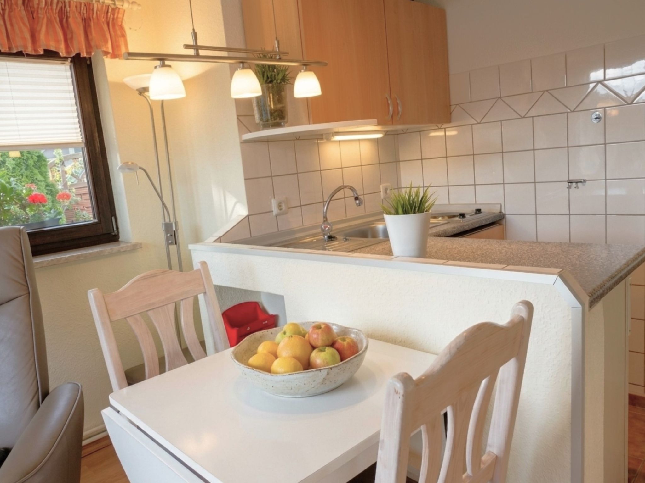 Eine Küche mit weißer Arbeitsplatte, einem Spülbecken und einer Obstschale auf einem Tisch.