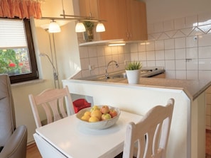 A kitchen with a white countertop, a sink, and a bowl of fruit on a table.