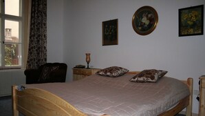 Ein Schlafzimmer mit einem hölzernen Bett, einem Nachttisch, einem Sessel und einem Fenster mit Vorhängen.