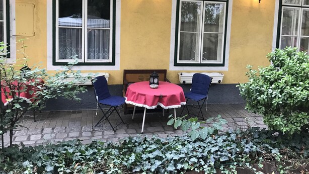 Ein gelbes Gebäude mit großen Fenstern und einem kleinen Tisch mit Stühlen davor.