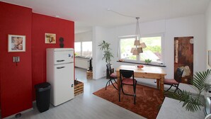 Una cocina moderna con un refrigerador blanco, paredes rojas y un comedor con una mesa y sillas de madera.
