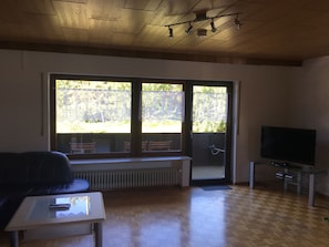 Relax in this spacious living room with a high ceiling and large windows offering a view of the lush outdoor area.