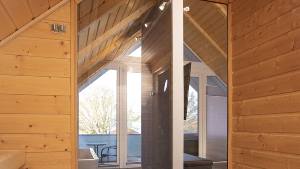 A wooden sauna room with a glass ceiling, a wooden bench, and a stone fireplace.