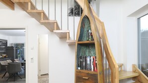 A modern interior with a wooden staircase, a bookshelf, and a dining area.