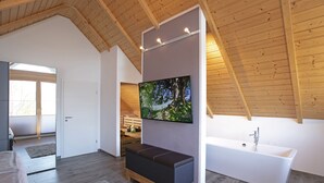 A modern bathroom with a bathtub, a wooden bench, and a large TV mounted on the wall.