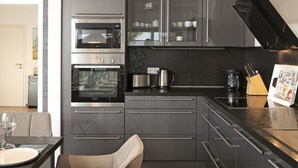 A modern kitchen with stainless steel appliances, a dining area with a table and chairs, and a wooden floor.