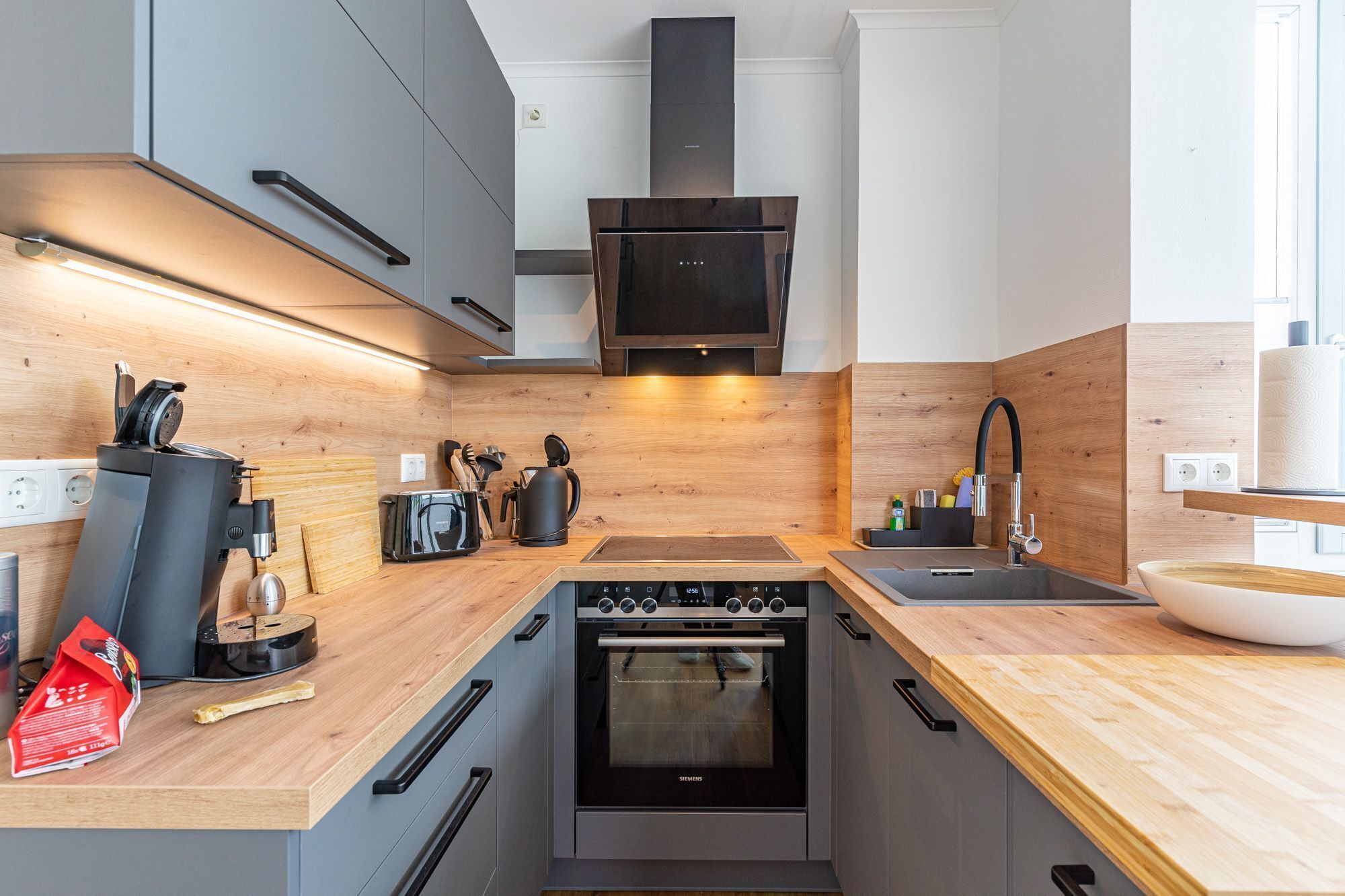 Eine moderne Küche mit grauen Schränken, Holz Arbeitsplatten, einem Einbauofen und einer schwarzen Dunstabzugshaube.