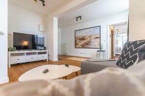 Un salon moderne avec un téléviseur à écran plat, un meuble de rangement blanc, une table basse ronde et un canapé gris.