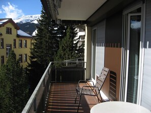 A balcony with a table and chairs, overlooking a snowy mountain and neighboring buildings. - First class 2 room apartment, 2-4 people, close to the center of congress (Graubünden)
