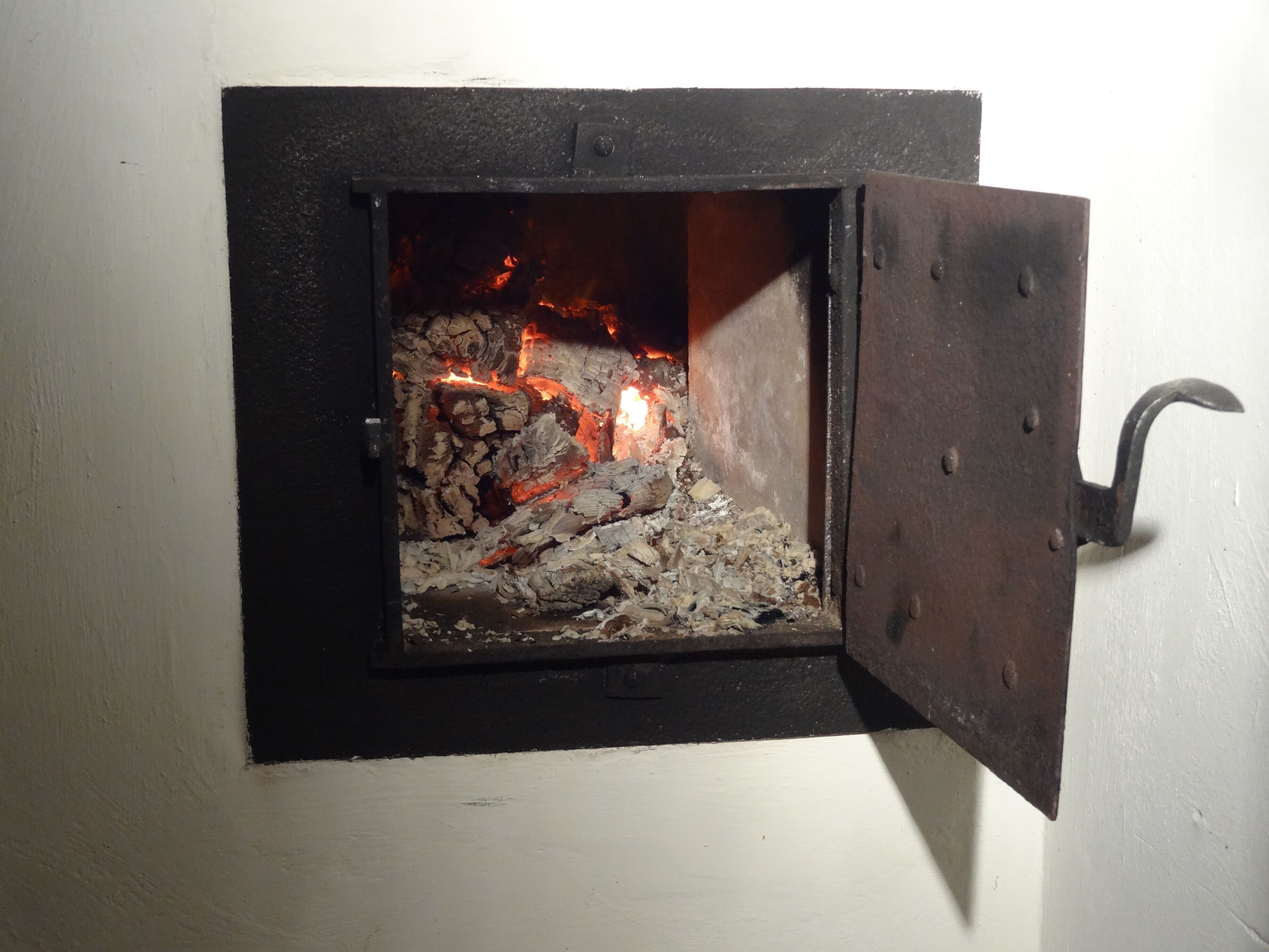 Une petite cheminée ouverte, avec des bûches qui brûlent à vue et une porte en métal.