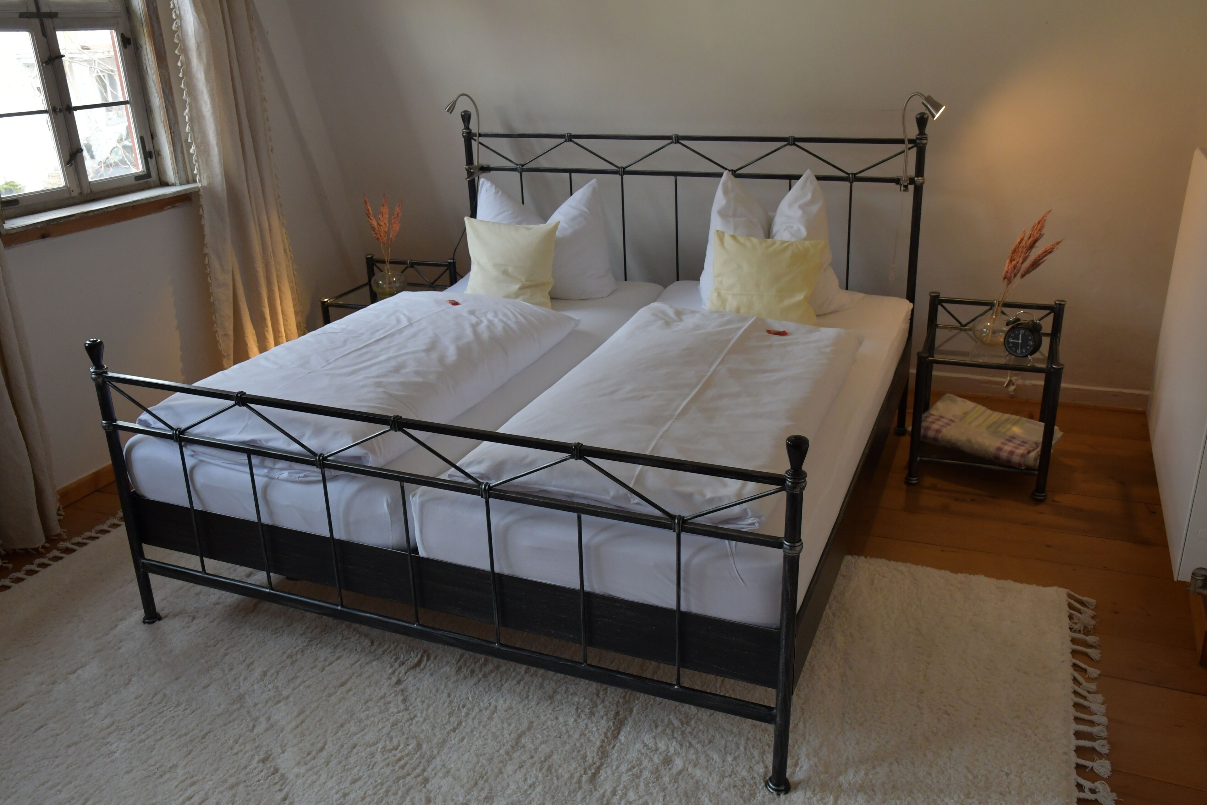 A bed with a metal frame, white bedding, and a small bedside table with a lamp.