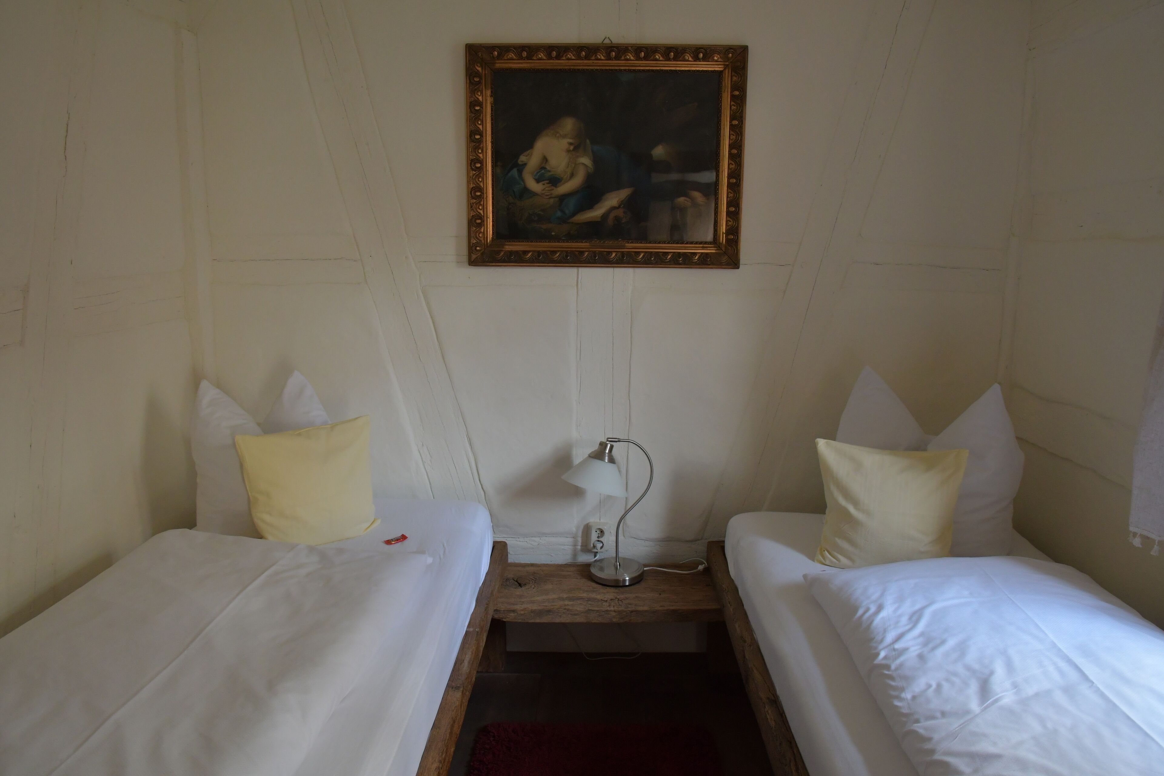 A room with two single beds, a nightstand with a lamp, and a painting on the wall.