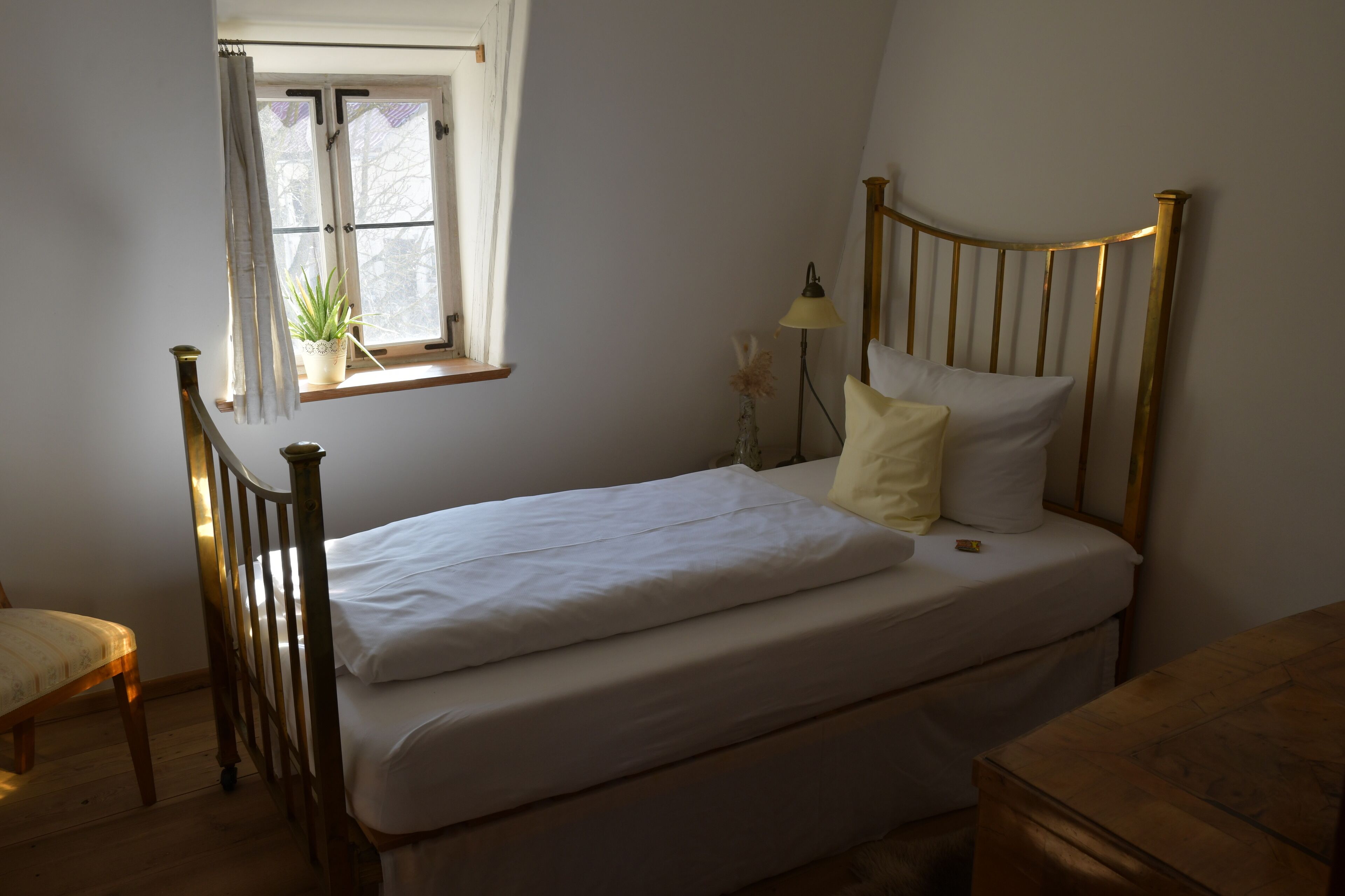 A bedroom with a wooden bed, a window with a plant, a bedside lamp, and a chair.