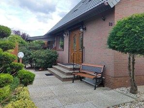 Ein Backsteinhaus mit Holztür, einer Bank davor und einem gepflegten Garten.