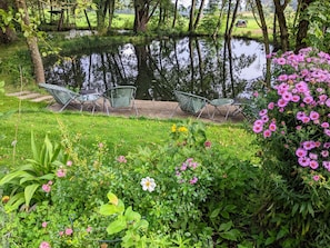 Un jardín tranquilo con un estanque, sillas y flores florecientes.