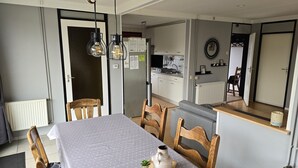 Comedor con mesa lista para cuatro, sillas de madera, mantel gris y una planta pequeña sobre una bandeja.
